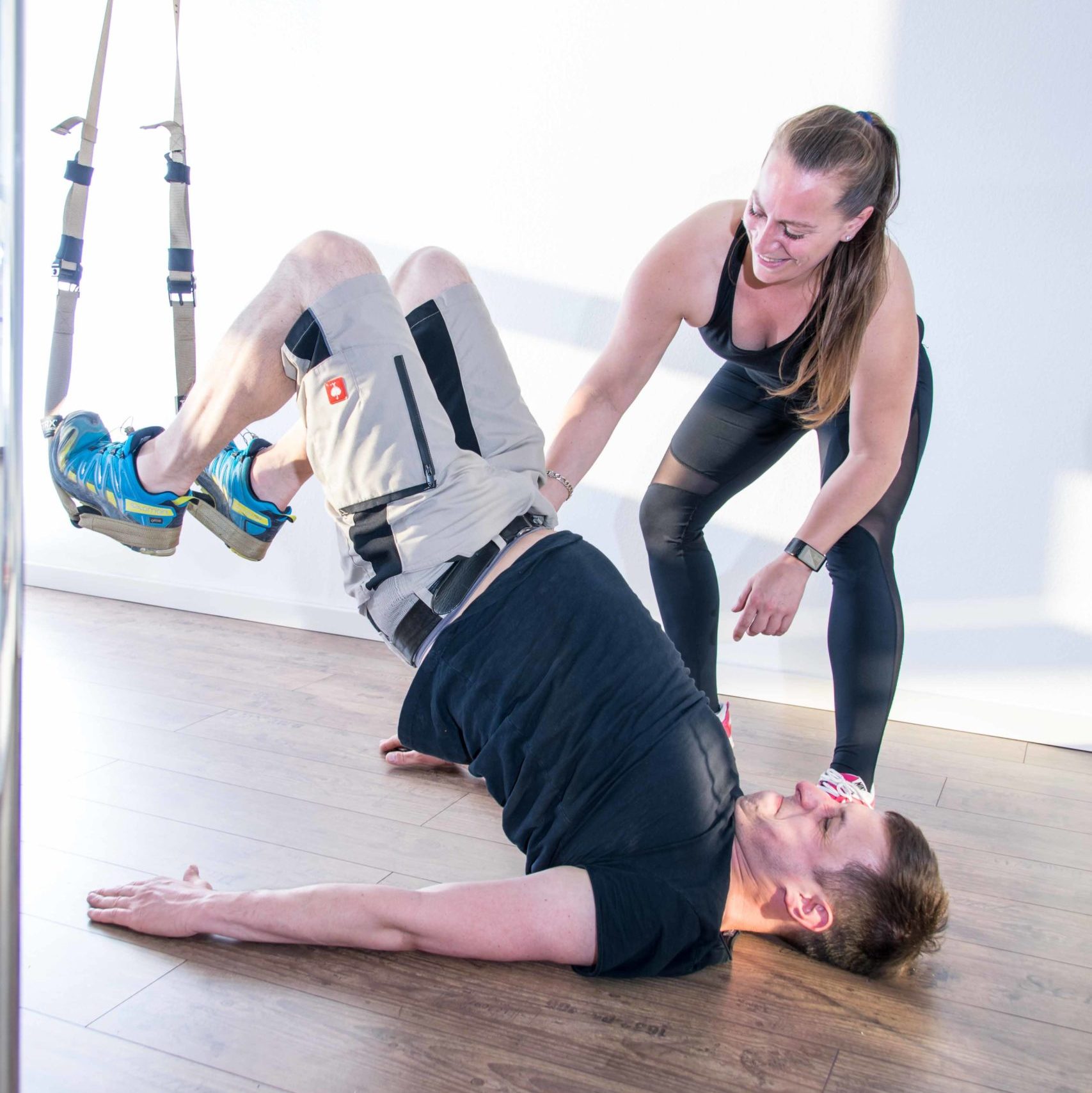 Personal Training UpsideDown Bad Homburg Frankfurt Bereich TRX Bänder. Theresa stabilisiert die haltung eines Schülers der die Füße in THX Bändern hat. UpsideDown Studio Bad Homburg nähe Frankfurt.